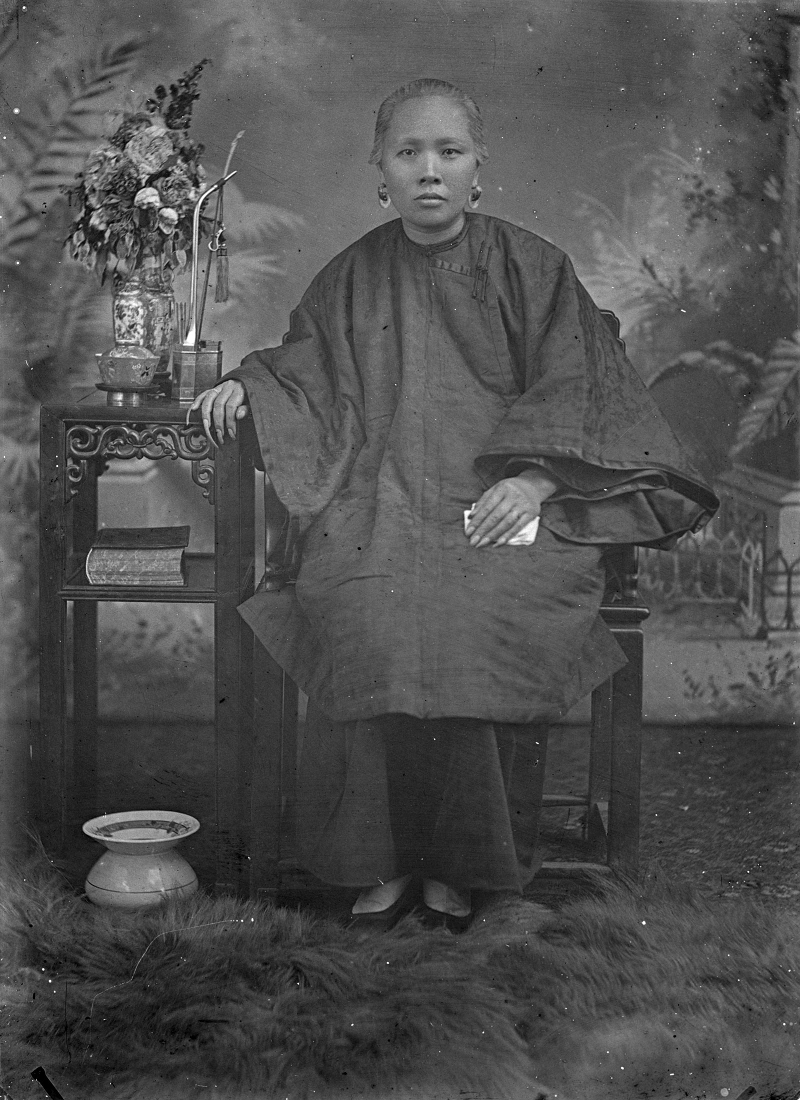 A photograph of a woman seated with flowers next to her.