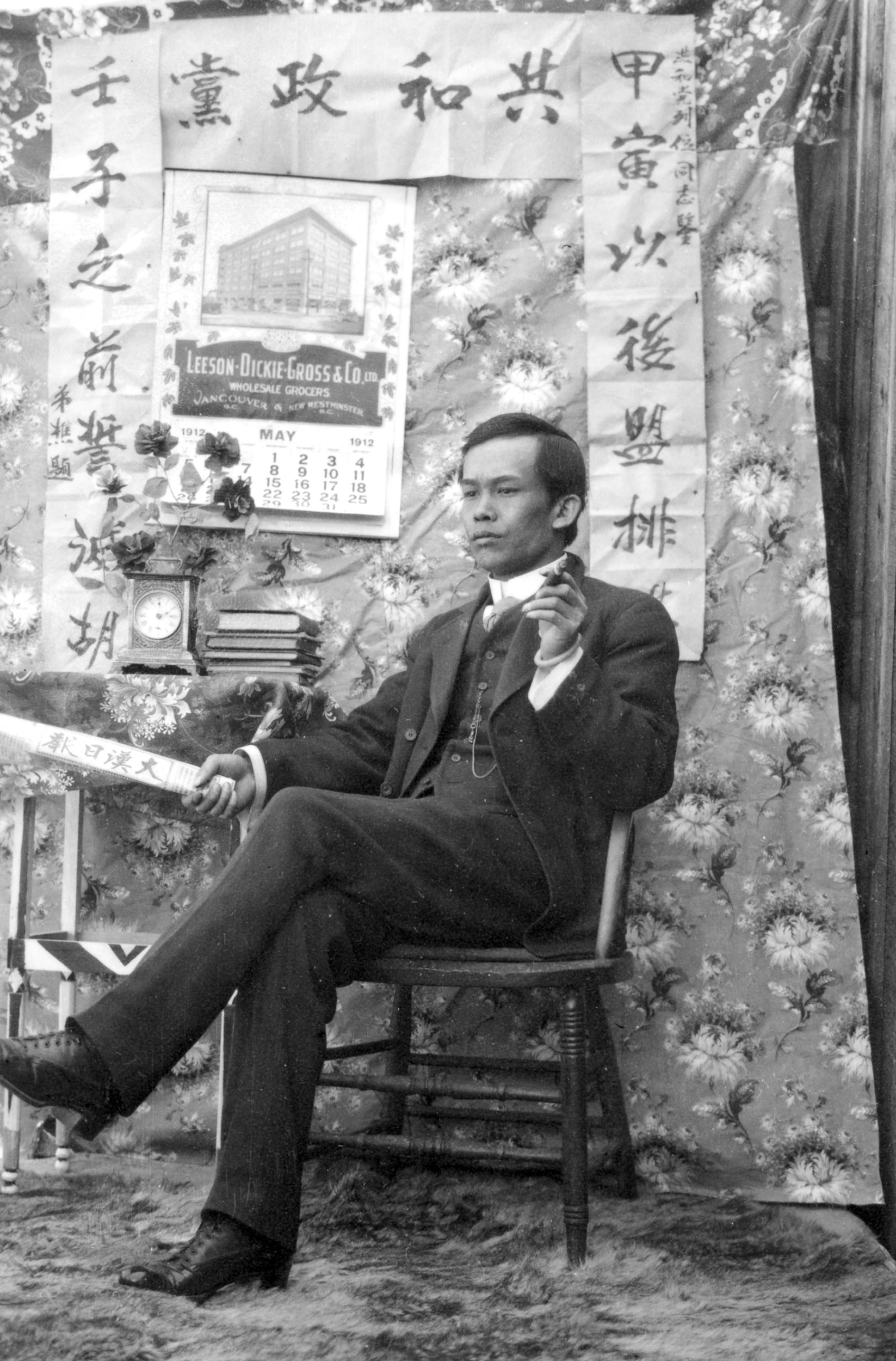 A black and white photo of a man in a suit seated with his legs crossed.